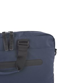 Bolso azul marino con una tela suave y resistente. Tiradores de cremallera dobles y un asa plana y texturizada. Forma rectangular compacta.