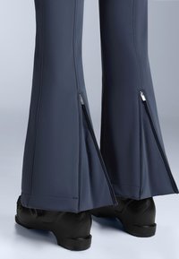 Morske rastezljive hlače s lepršavim rubom, s bočnim patentnim zatvaračima na donjim dijelovima nogavica. Materijal izgleda glatko, u kombinaciji s crnom obućom.