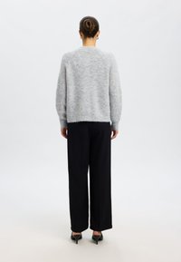 Világosszürke kötött pulóver, kényelmes fazonban, bordás mandzsettákkal, fekete, bő szárú nadrággal és hegyes orrú fekete magassarkú cipővel párosítva.