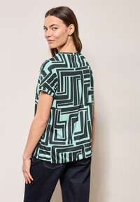 Kortærmet mintgrøn t-shirt med et iøjnefaldende sort geometrisk mønster, afslappet pasform og rund halsudskæring.