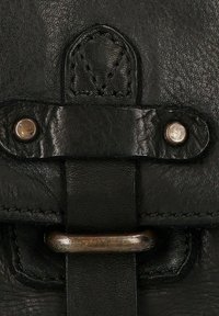 Dettaglio di una borsa in pelle nera con superficie testurizzata, hardware in tonalità argento, accenti cuciti e una cinghia centrale con un anello metallico.