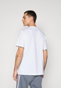 T-shirt med kortærmer og rund hals i hvid bomuld. Har en afslappet pasform med glat tekstur og lige kant. Ingen synlige mønstre eller detaljer.