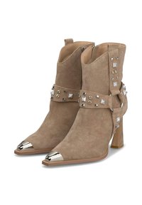 Botines de ante beige con punta afilada, puntera metálica plateada, correa decorativa con tachuelas y strass, y un alto tacón cuadrado.