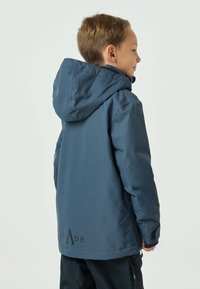 Giacca blu navy con cappuccio. Presenta una texture liscia e un dettaglio logo sull'orlo posteriore. Progettata per comfort e protezione.