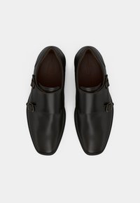 Sapatos de couro pretos com um acabamento liso, apresentando duas fivelas metálicas e um design de bico arredondado. A sola é plana e texturizada.