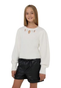 Biały sweter dziany z okrągłym dekoltem i akcentami w kształcie dziurki, w połączeniu z czarnymi szortami z sztucznej skóry z wywiniętym dołem.
