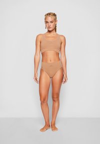 Beige Sport-BH und hochtaillierte Bikinihose aus glattem Stoff. Minimalistisches Design und dezentes Markenlogo in Grau.
