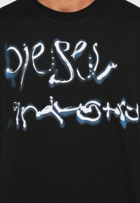 Μαύρο βαμβακερό t-shirt με λευκό και μπλε αφηρημένο κείμενο, στρογγυλή λαιμόκοψη και κοντά μανίκια, με λεία υφή.