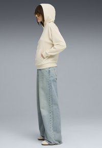 Cremefarvet ribbet hoodie med en lomme foran, parret med lyseblå vide jeans. Hætten er fastgjort, og ærmerne er manchetteret.