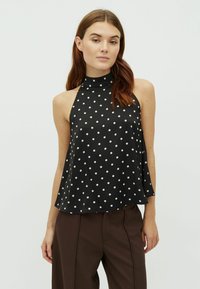 Čierny top na traky s bielymi bodkami, vysokým povrchom a voľným strihom s hladkou textúrou. V kombinácii s hnedými nohavicami.