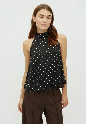 Haut à col halter noir avec des pois blancs, un col haut et une coupe décontractée avec une texture lisse. Associé à un pantalon marron.