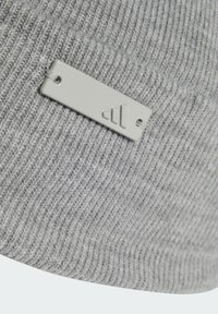 Sivi pleteni šešir s teksturiranom tkaninom, s pravokutnom sivom oznakom koja prikazuje minimalistički logo i rupom za pričvršćivanje.
