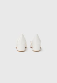 White heeled shoes with a smooth leather texture, featuring a tapered design and a block heel. The sole is light brown.