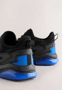 Zwarte sportschoenen met blauwe accenten, een gestructureerde rubberen zool, een gevoerde rand en een aantreklus. Glad materiaal met contrasterende designdetails.