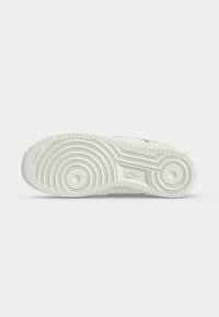 Σόλα ενός λευκού αθλητικού παπουτσιού Nike με κυκλικά σχέδια πέλματος και το λογότυπο της Nike στη μέση, σε απλό φωτεινό φόντο.