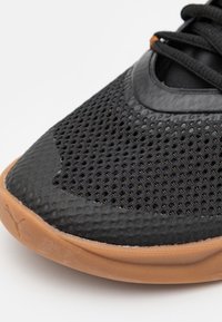 Nahaufnahme der Schuhspitze eines schwarzen Mesh-Sneakers mit brauner Gummisohle und schwarzen Schnürsenkeln, die Struktur und Belüftungsdetails zeigt.