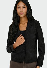 Blazer en velours côtelé noir avec un col à revers, fermeture à un bouton et poches avant. Texture lisse et design ajusté.