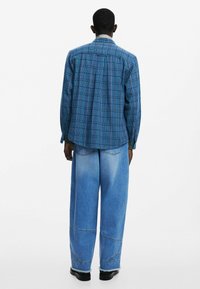 Niebieska koszula w kratkę z materiału, z długimi rękawami, luźny krój. Połączona z jasnoniebieskimi dżinsami z szerokimi nogawkami, z widocznym przeszyciem i postrzępionymi końcami.