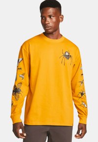 Tricou cu mânecă lungă, de culoare galbenă, din bumbac, având grafica unor insecte negre pe față și pe mâneci. Design standard cu guler rotund.