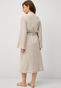 Beige waffle-structuur badjas met lange mouwen, een ceintuur in de taille en een lengte tot de knie, met een eenvoudig, minimalistisch ontwerp.