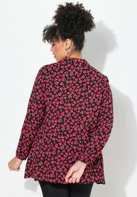 Langärmlige Bluse mit schwarzem Hintergrund und rotem Herzmuster, leichtes Material und entspannte Passform mit abgerundetem Saum.