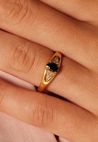 Gouden ring met een centrale zwarte steen, omringd door driehoekige accenten met kleine heldere stenen. Glad oppervlak met een gepolijste afwerking.