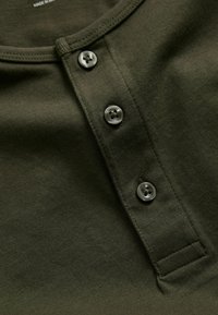 Dark green shirt fabric with three black buttons on a placket near the rounded neckline.