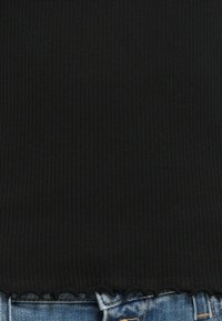 Zwarte geribbelde top met een golvende zoom, gemaakt van een zachte stof. De onderrand is iets rafelig en wordt gedragen met lichtblauwe denimshorts.