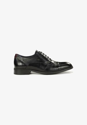 Zapato Oxford de hombre de cuero negro con puntera con costura, cordones cerrados, tacón bajo y detalle granate en la lengüeta del talón.
