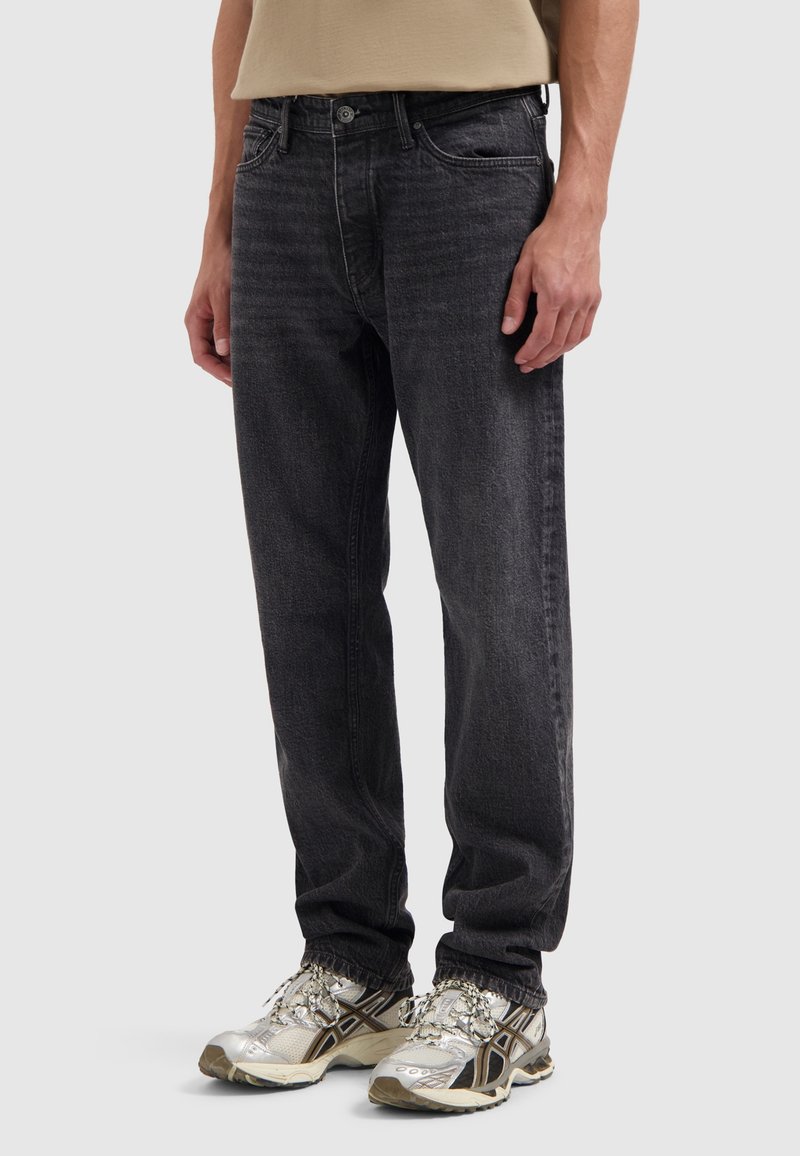 Zwarte denim jeans met een relaxte pasvorm, vijf zakken, subtiele wassing en een licht vervaagde afwerking, gecombineerd met zilveren sneakers.