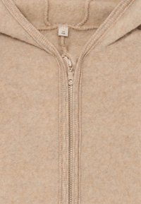 Bežna polarna zip-up kapuca z mehko teksturo, z metalnim zadrgo in kapuco z vrvico. Notranja oznaka vidna na vratu.