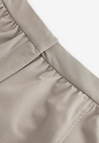 Morseau de tissu gris clair en gros plan avec une ceinture élastique froncée. Texture lisse et détail de couture précis visible le long des coutures.