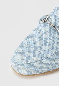 Ανοιχτό μπλε παπούτσι από υφασμάτινο τζιν με υφή, διακοσμημένο με λουλούδια και ασημένιες λεπτομέρειες. Διαθέτει στρογγυλή μύτη και επίπεδη σόλα.