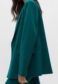 Turkusowa marynarka o strukturalnym kroju, z klapami w kształcie notcha, przednimi kieszeniami i dopasowanym fasonem, wykonana z gładkiego materiału.