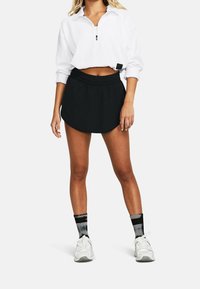 Bílý žebrovaný top s dlouhým rukávem a zipovým límcem, černá sukně s šortkami. Sukně má volný střih a hladkou texturu. Nosit spolu s bílými teniskami a vzorovanými ponožkami.