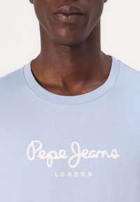 Ανοιχτό μπλε βαμβακερό μπλουζάκι με στρογγυλή λαιμόκοψη και κοντά μανίκια. Διαθέτει λευκό λογότυπο γραμμένο "Pepe Jeans LONDON" στο στήθος.
