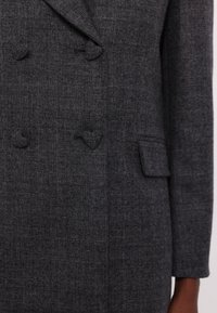 Doppelt gefütterte graue Blazerjacke aus strukturiertem Stoff, mit zwei herzförmigen Knöpfen und einer seitlichen Tasche. Minimalistisches Design, strukturierte Passform.