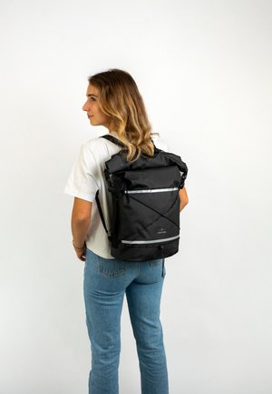 Fekete, felgörgethető hátizsák állítható pántokkal, fényvisszaverő részletekkel és texturált nylon anyagból készült, világos háttéren elhelyezve.
