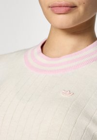 Pull en tricot avec un corps crème, un col côtelé rayé rose clair et un petit logo brodé rose sur le devant.