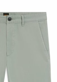 Jasnozielone spodnie wykonane z gładkiego materiału, z zapięciem na guziki, przednimi kieszeniami i starannym wykończeniem szwów.