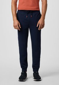 Marine joggerbroeken gemaakt van glad stof met een elastische tailleband en trekkoord. Kenmerken zijn mouwen met elastiek aan de enkels en zijzakken. Gecombineerd met zwarte sneakers.