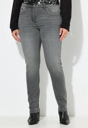 Jeans skinny grises con bolsillos, adornados con tachuelas plateadas. Textura de denim con un ligero desgaste; combinados con botines negros de tacón.