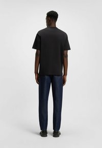 Maglietta nera a maniche corte con taglio dritto, abbinata a pantaloni in denim blu scuro, con vestibilità classica e design minimalista.