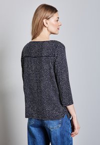 Marinblus med mönstrade vita prickar och linjer, med trekvartslånga ärmar och rak passform, i kombination med blå denimjeans.