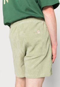 Lichtgroene badstof shorts met een elastische tailleband, voorzien van een achterzak en een klein rood label. Soepele textuur en losse pasvorm.