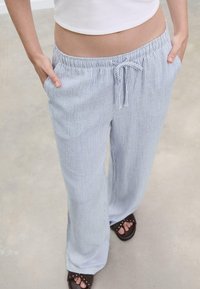 Pantalons à rayures bleu clair et blanches, ample, avec un waistband élastique et un cordon de serrage. Comprend des poches latérales et un design décontracté.