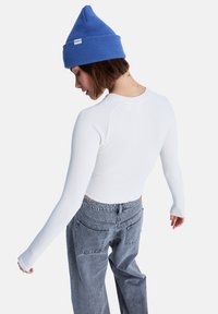 Λευκό ριμπ μακρυμάνικο τοπ με στρογγυλή λαιμόκοψη, συνδυασμένο με ψηλόμεσο γκρι denim παντελόνι και μπλε ριμπ πλεκτό σκουφάκι.