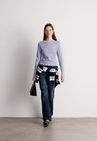 Ανοιχτό μωβ πουκάμισο με μακρύ μανίκι, μπλε τζιν και μία μαύρη τσάντα, με ένα λευκό και ναυτικό σχέδιο πουλόβερ δεμένο στη μέση.