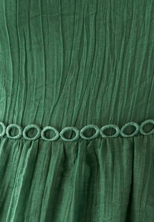 Green fabric dress with textured waves, featuring a decorative looped trim at the waistline. Made of lightweight, flowing material.