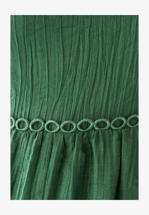 Vestido de tela verde con ondas texturizadas, que presenta un ribete decorativo en forma de bucle en la cintura. Está hecho de un material ligero y fluido.